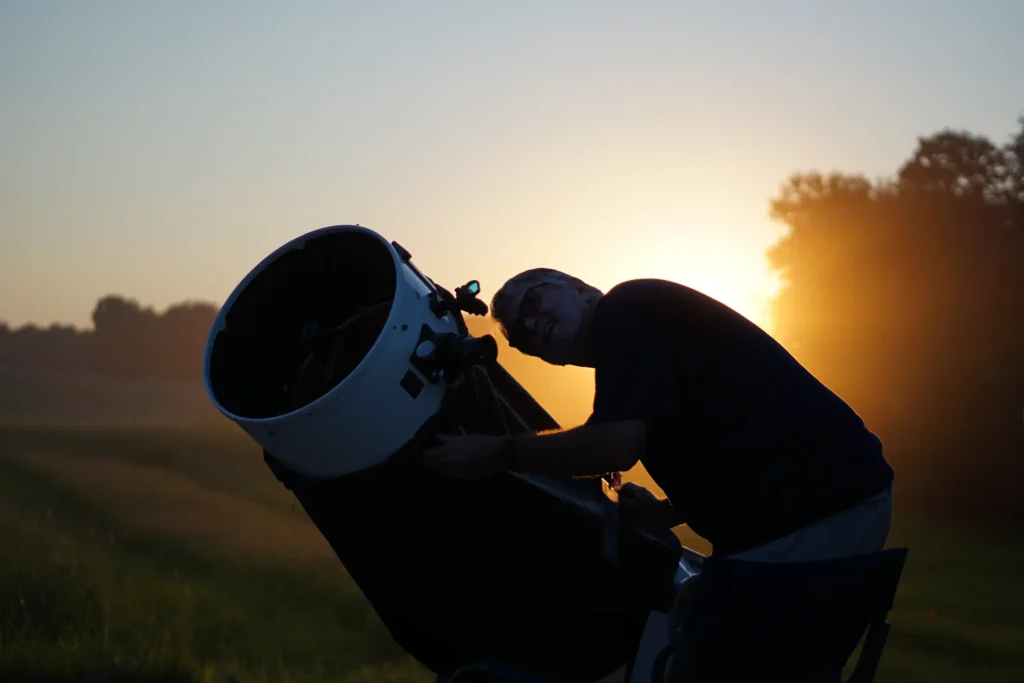 Man looking through telescope at dusk.